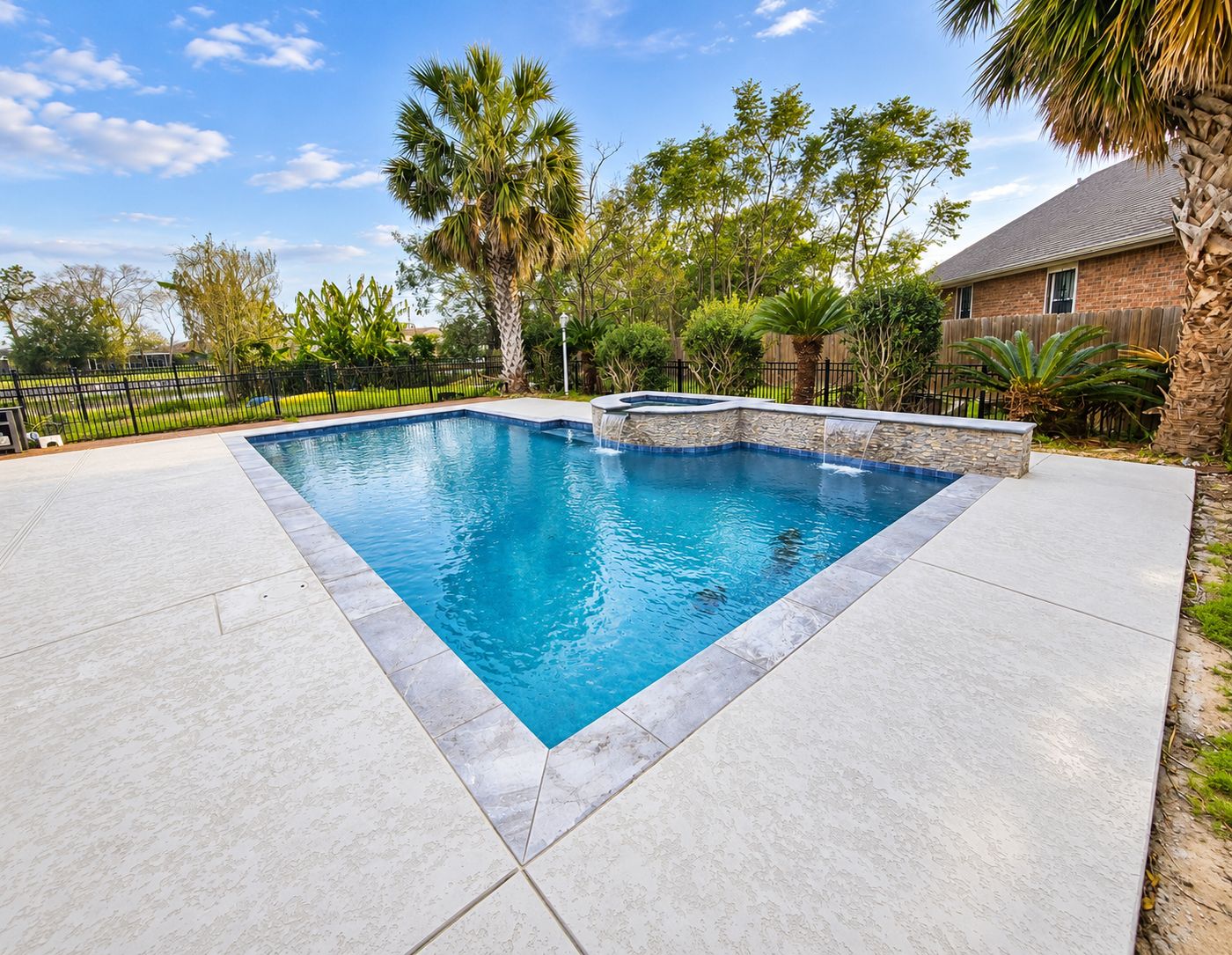 After: the same pool with clear blue water, gray stone coping, a coated deck, and a stacked-stone spa wall