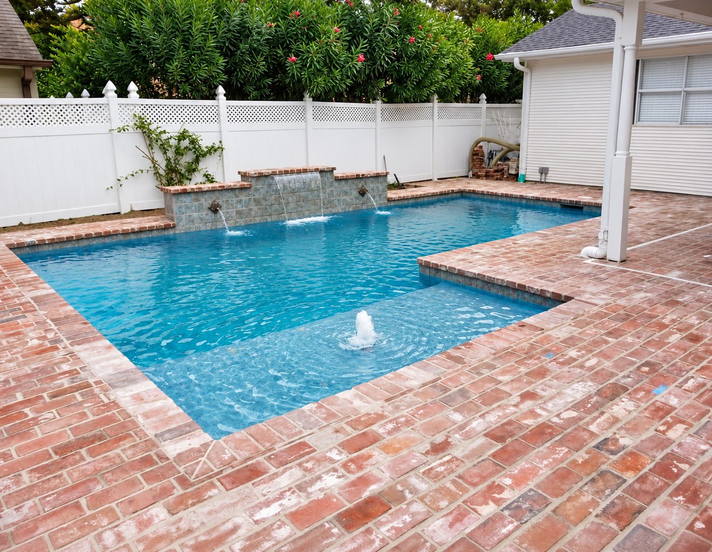Rectangular pool with a sun shelf bubbler, a tiled water-feature wall with a sheer descent and two scuppers, and a reclaimed brick deck