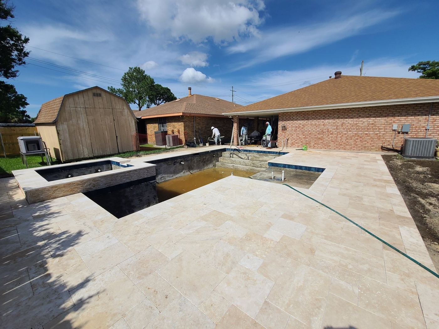 Step 11 of 14, Deck: Travertine deck laid around the pool, with stacked stone on the spa wall.