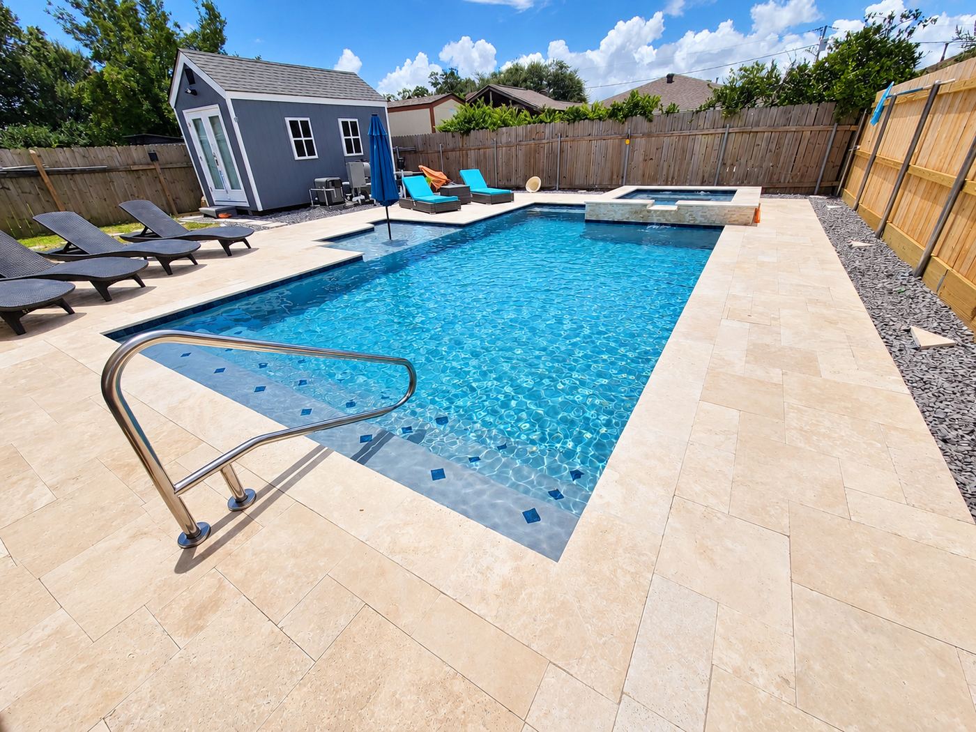 Rectangular pool with travertine deck, tiled steps, handrail, loungers, and a sun shelf umbrella