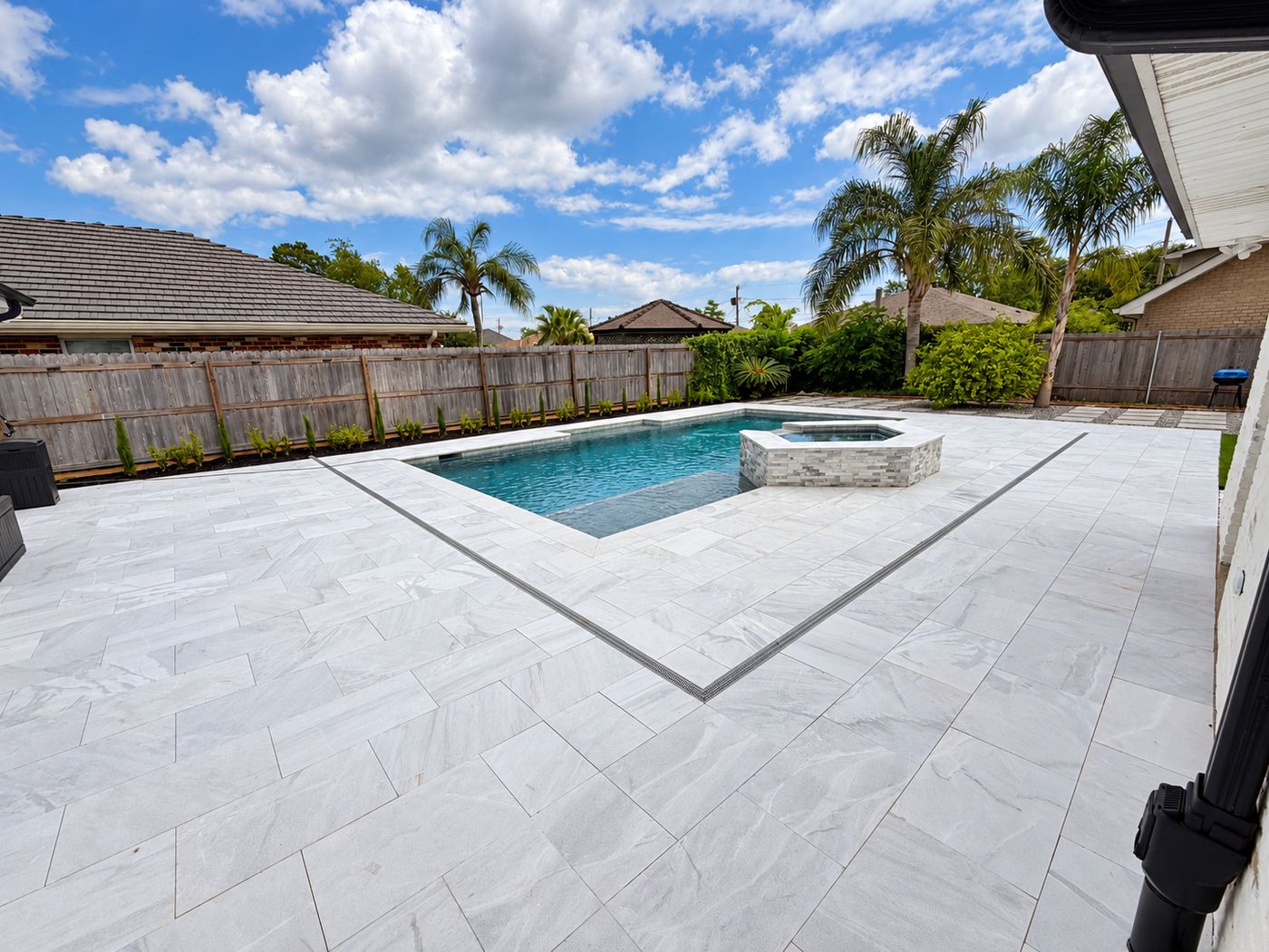 Pool and raised spa surrounded by a large light gray stone deck with a linear drain