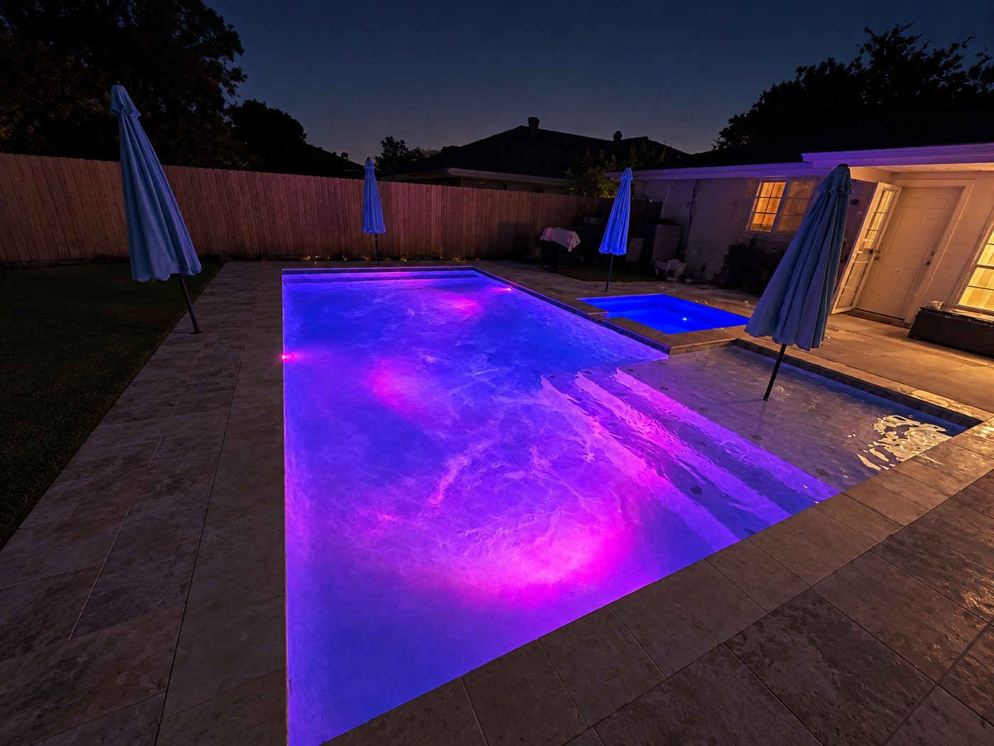 Rectangular pool, sun shelf, and raised spa lit purple and blue at night with color-changing lights
