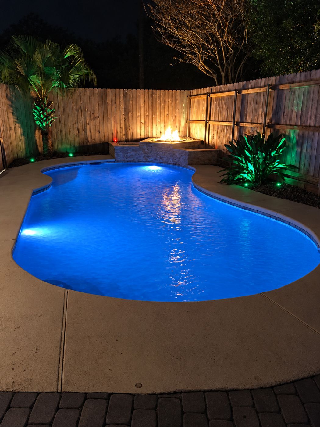 Freeform pool lit at night with a stacked-stone fire feature