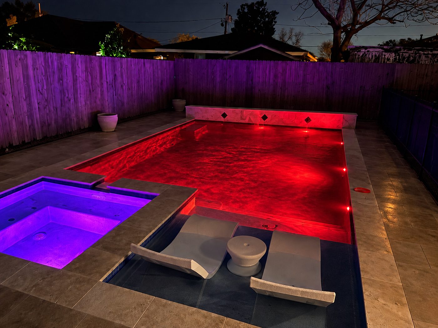 Pool lit red and spa lit purple at night, with in-pool loungers on the sun shelf