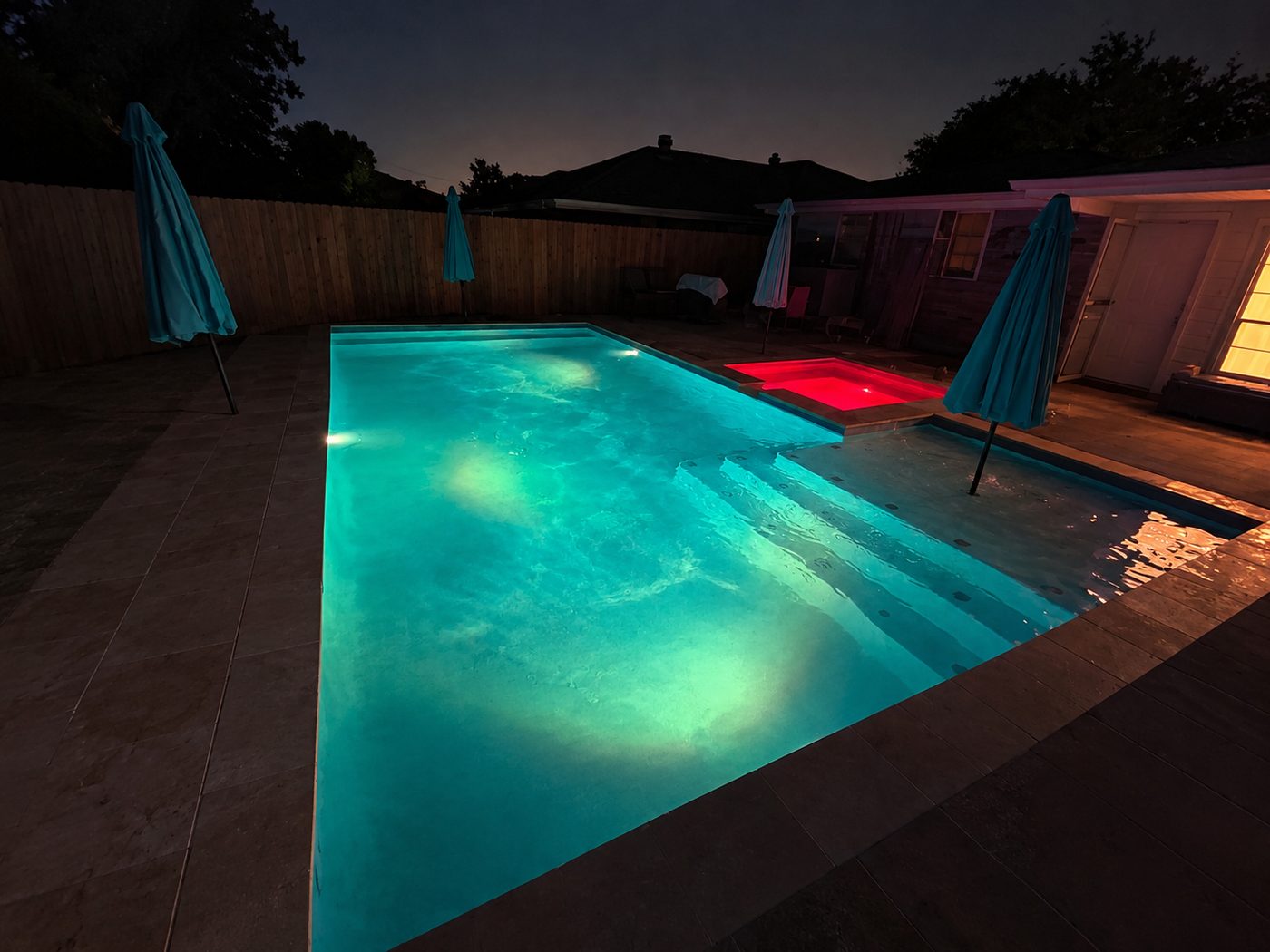 Pool glowing teal at night beside a raised spa lit red, showing the color-changing lights