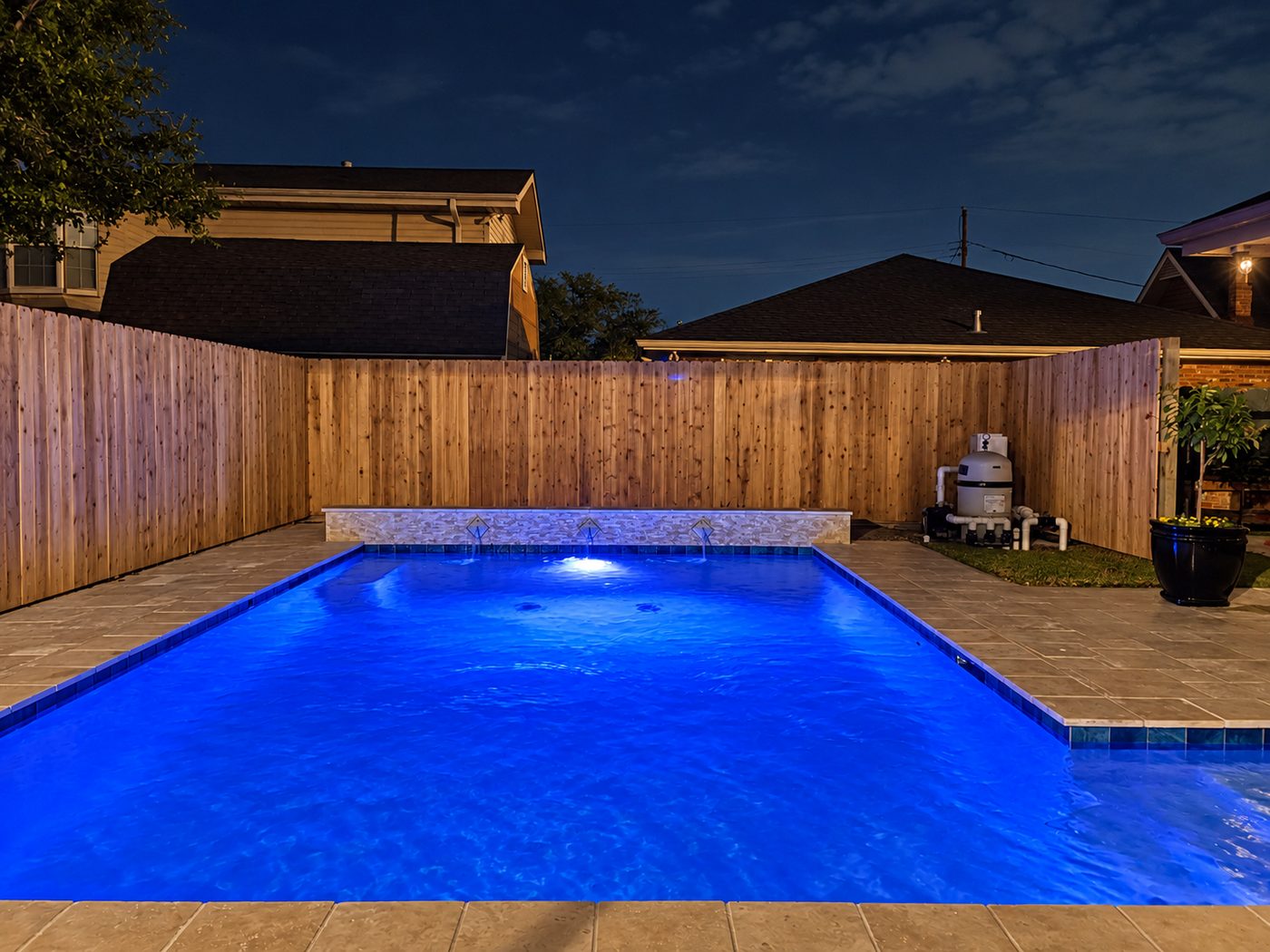 Rectangular pool lit blue at night, with a stacked-stone wall and three sheer water features