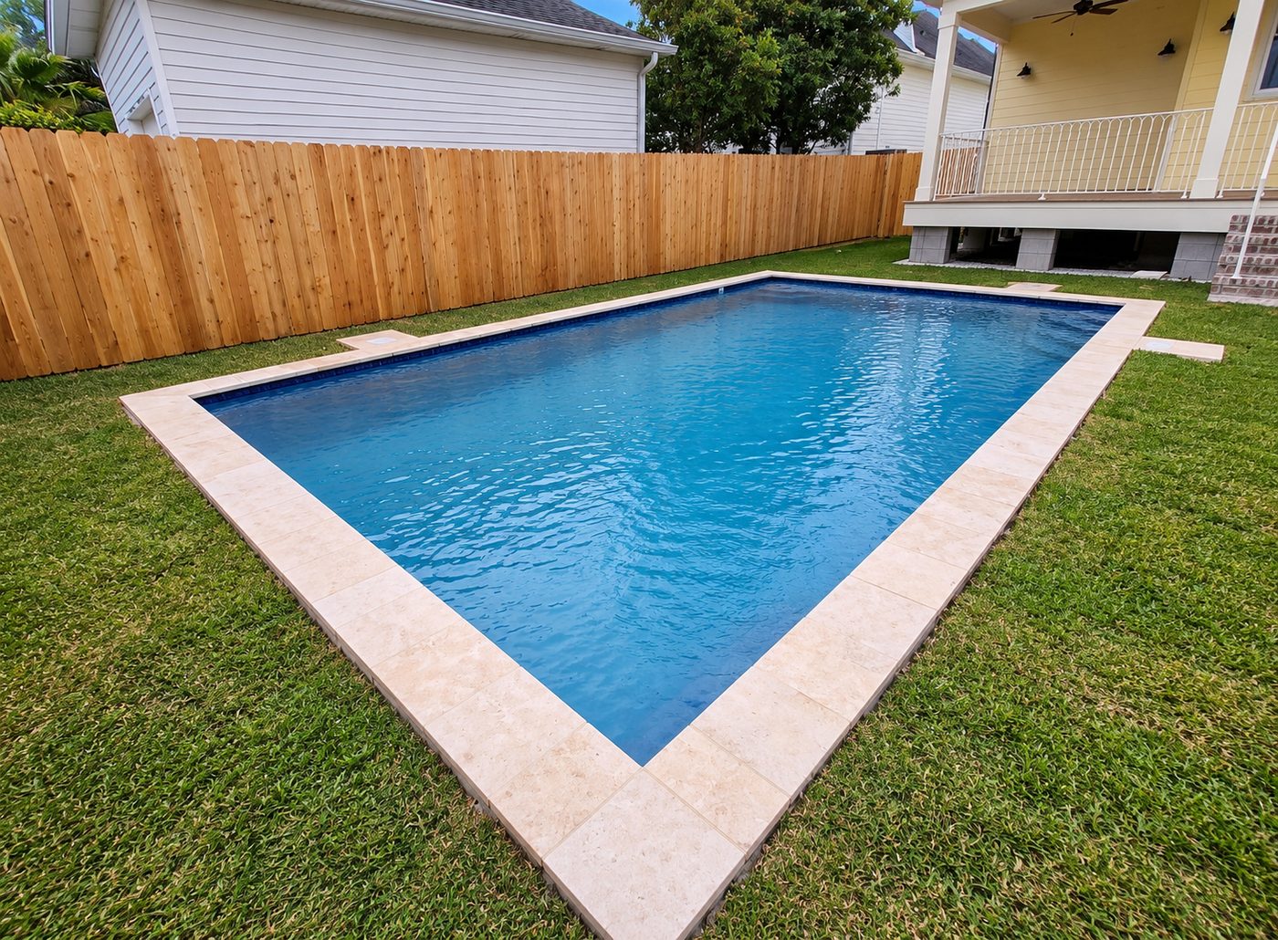 Rectangular pool with light stone coping set into a grass lawn, beside a yellow raised home and a new wood fence