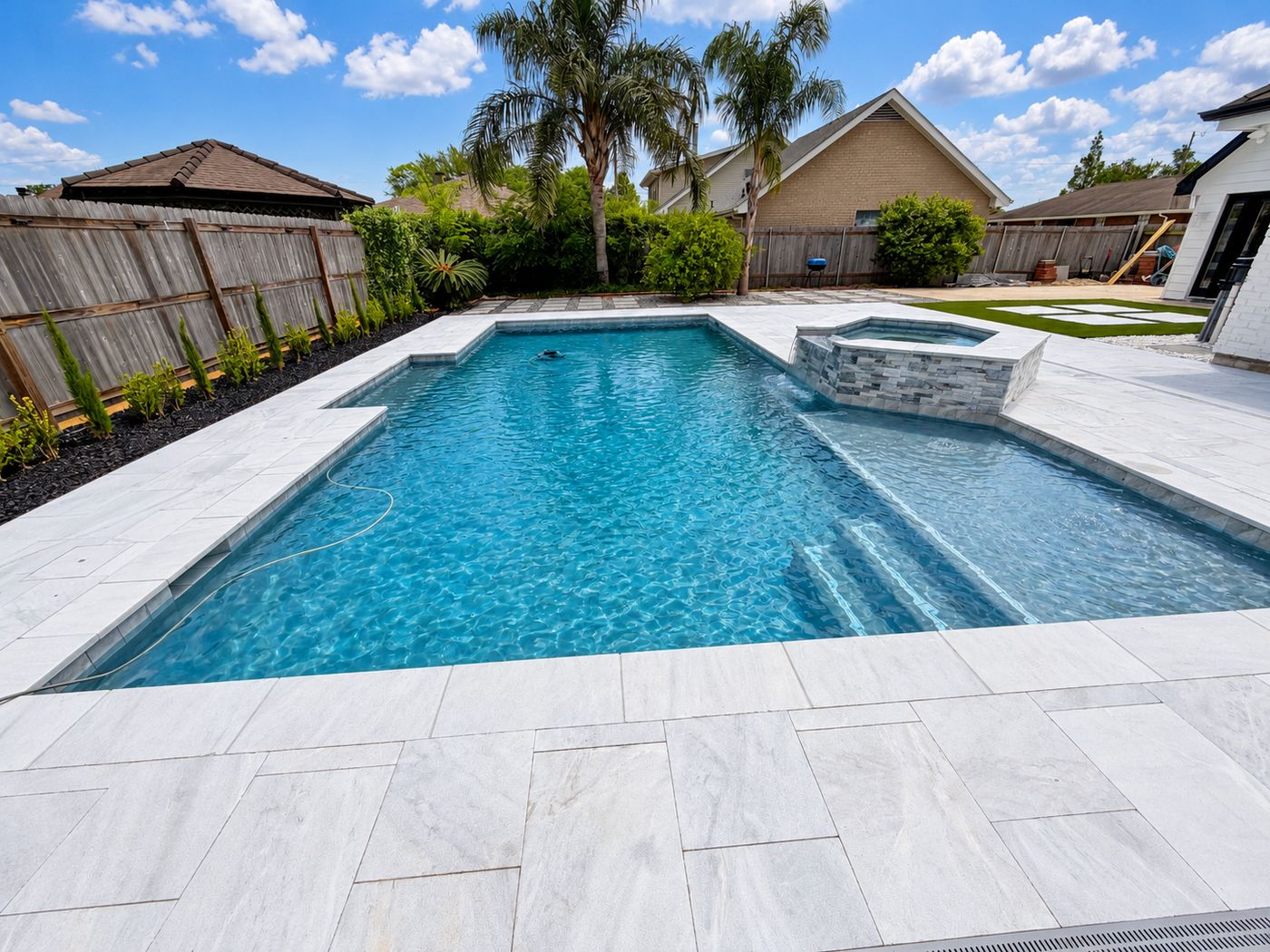 Rectangular pool with a sun shelf, steps, and a stacked-stone raised spa, surrounded by a light stone deck